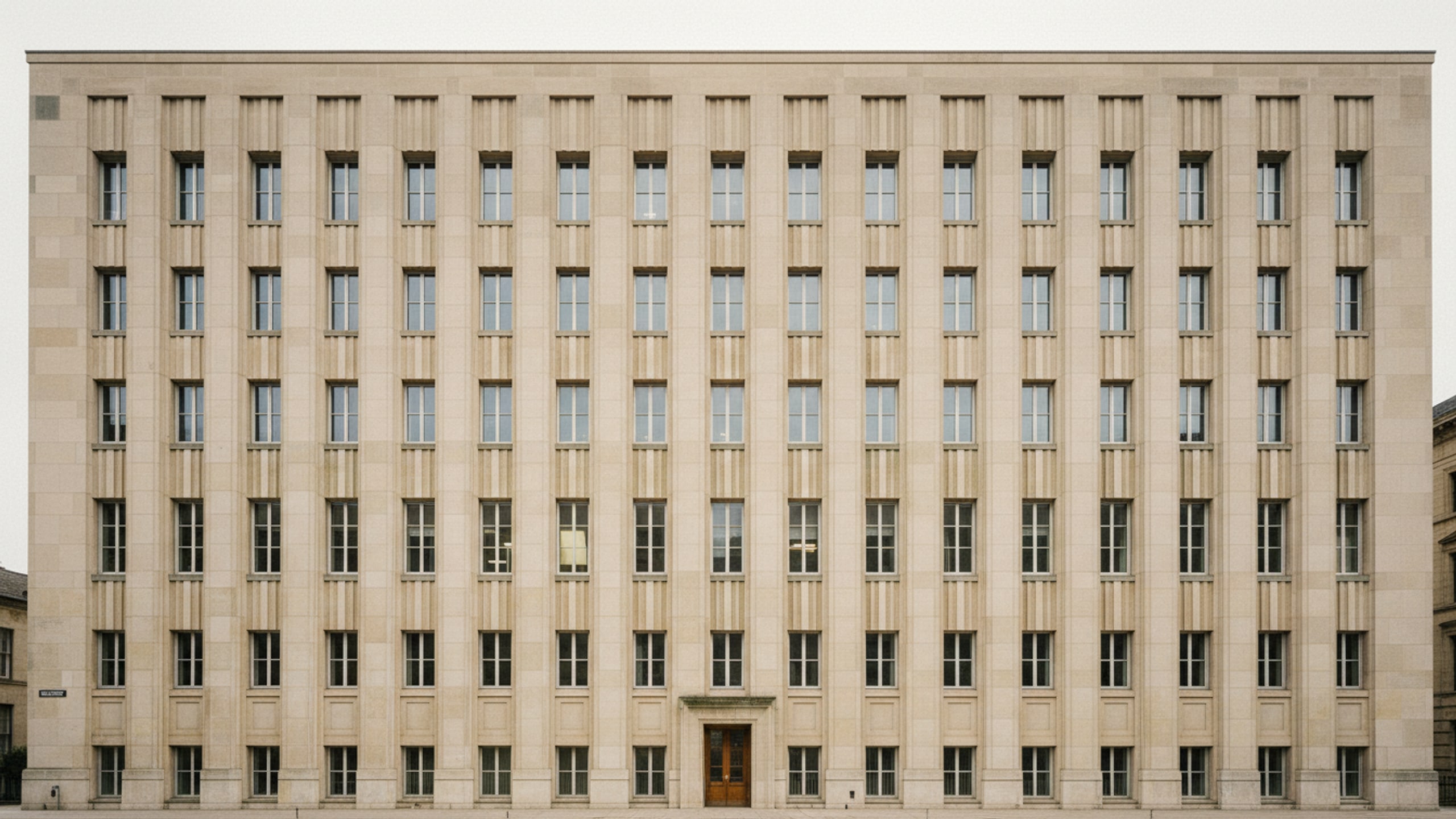 Stone civic facade in flat morning light, deep shadow under a plain cornice