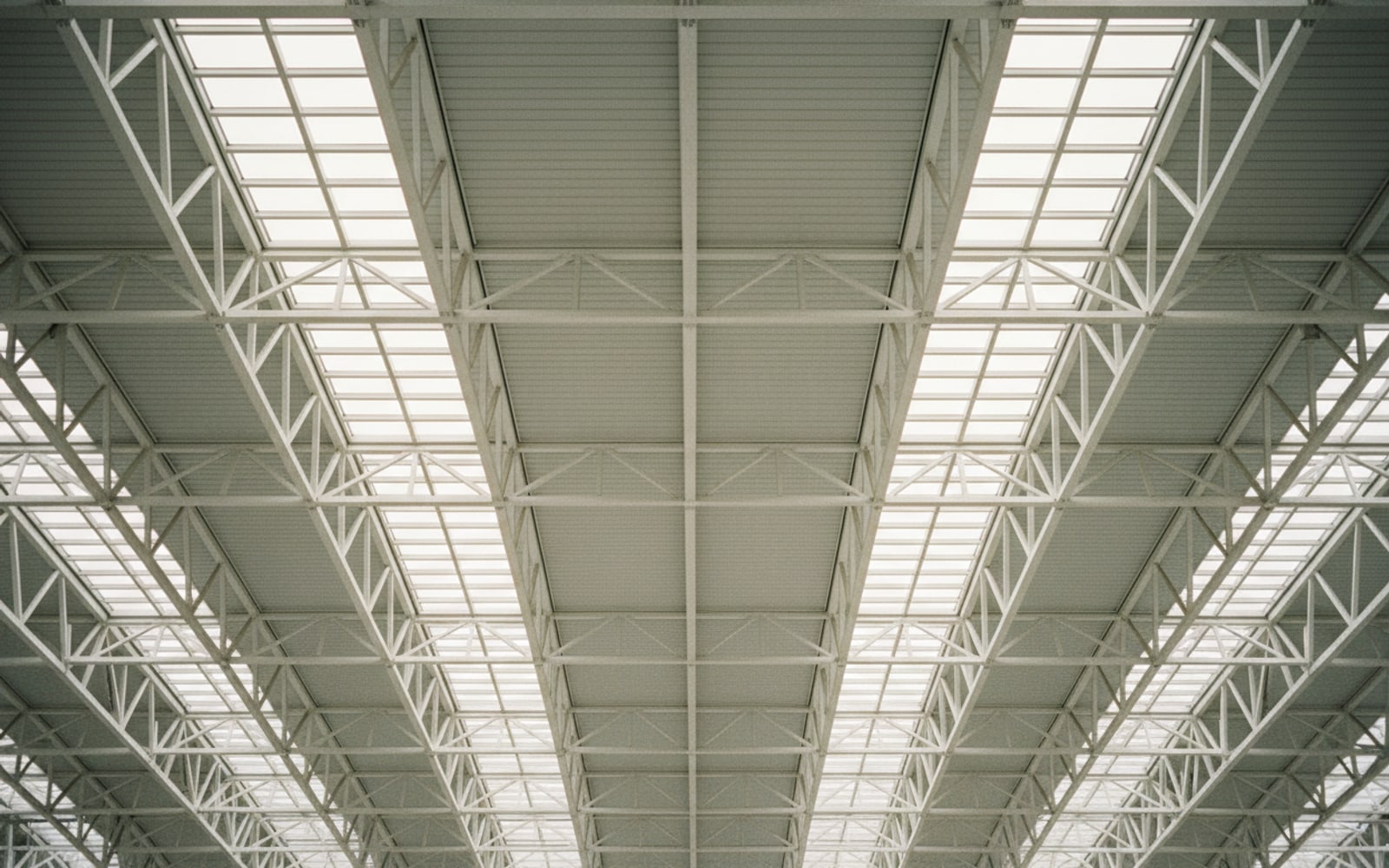 Airport terminal roof structure seen from beneath, repeating steel trusses and skylights